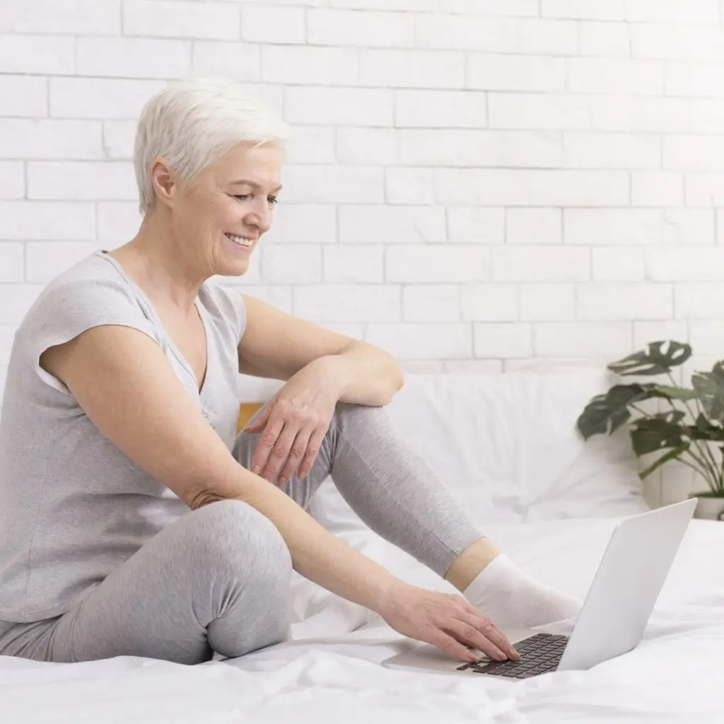 Cheerful senior lady enjoying internet on laptop at home